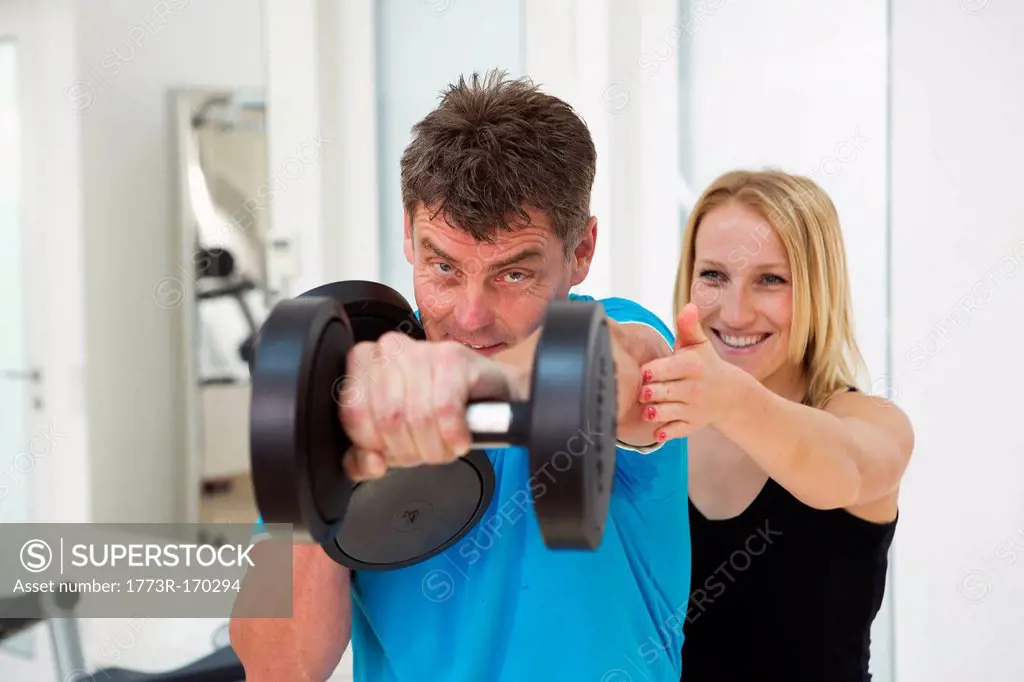Trainer adjusting mans form in gym