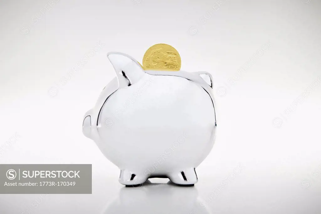 Gold coin dropping into piggy bank