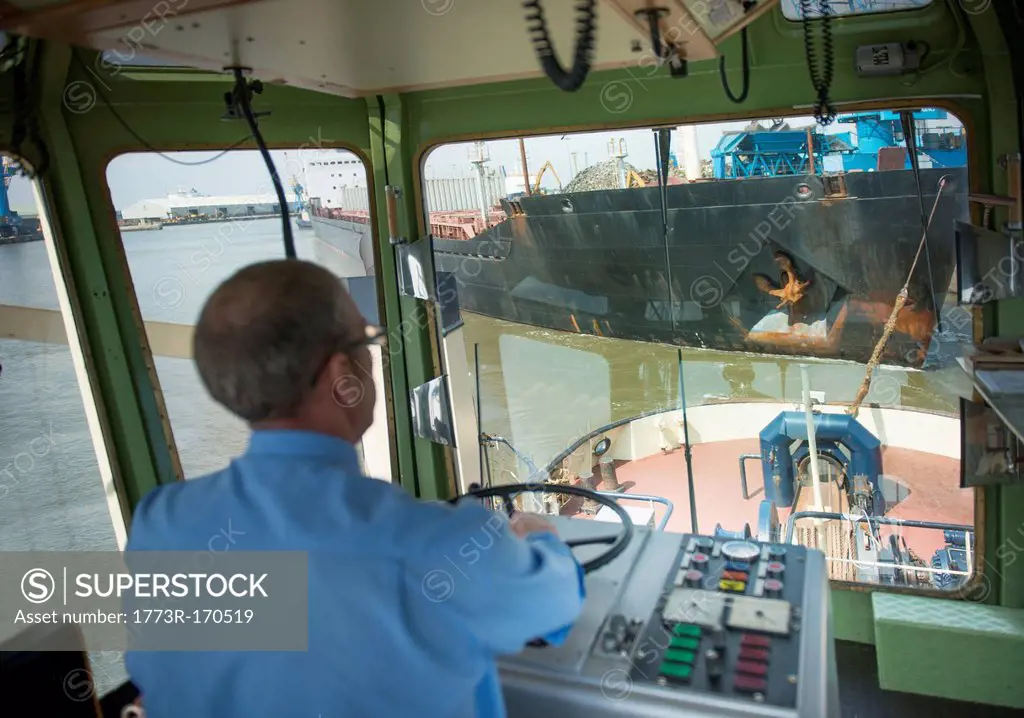 Captain steering tugboat in wheelhouse
