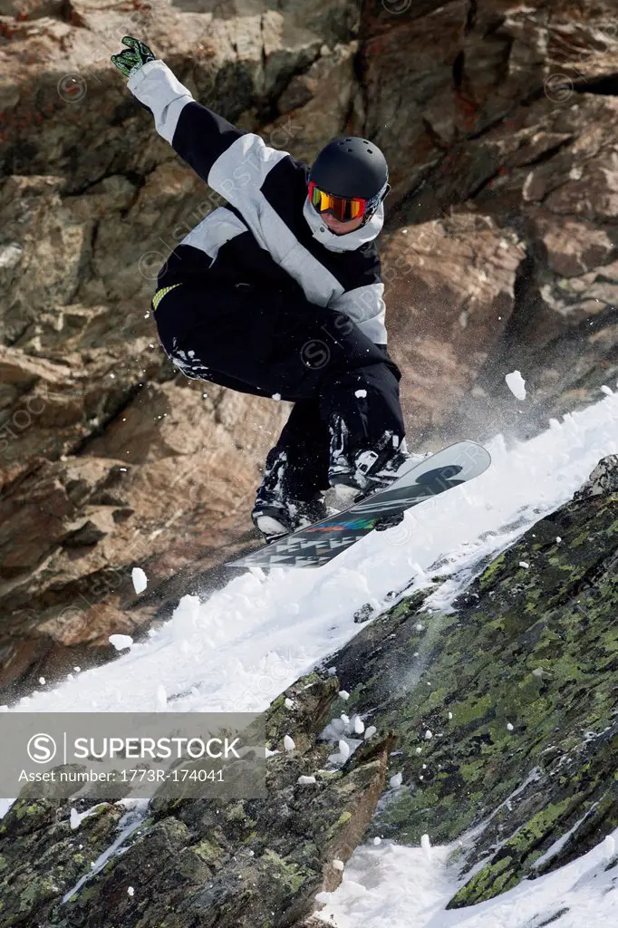 Snowboarder jumping on rocky slope