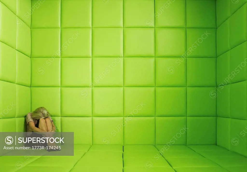 Woman crouching in corner of green padded cell