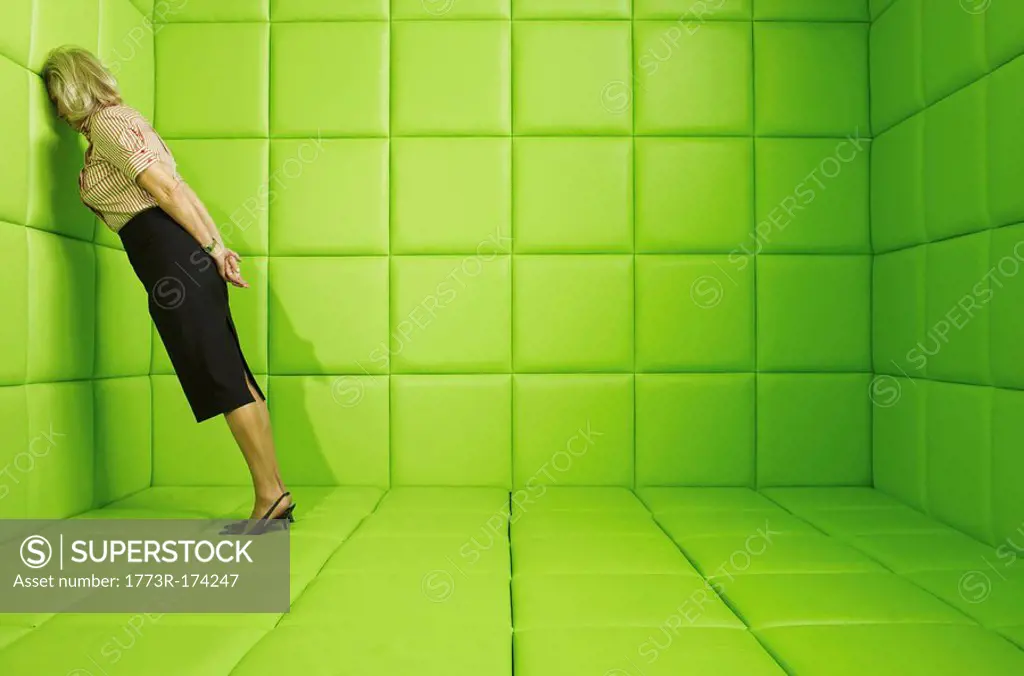 Woman leaning head against wall in a green padded cell