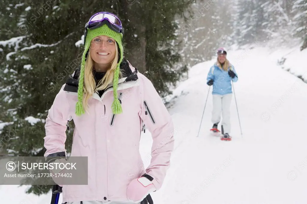 Young woman smiling on ski-slope, person in background on snow-shoes, portrait