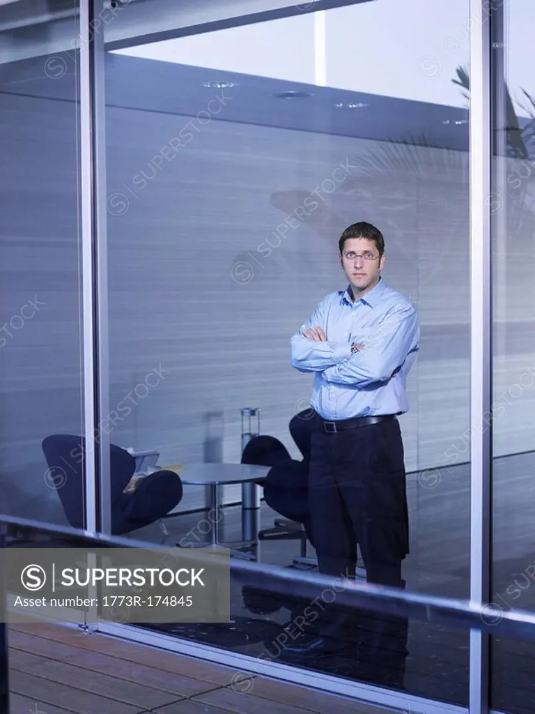Young businessman standing at window in office, portrait