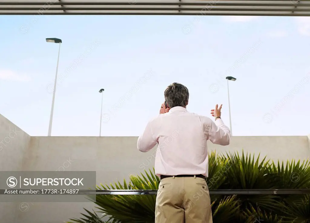 Man standing on balcony using mobile phone, rear view