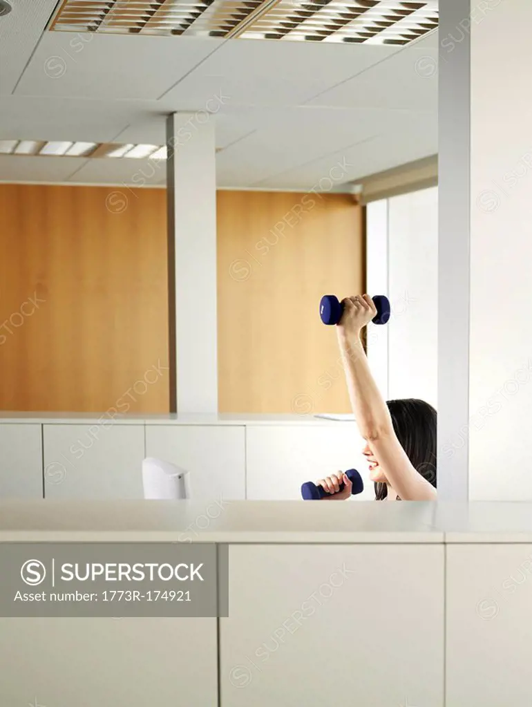 Woman sitting in office lifting weights