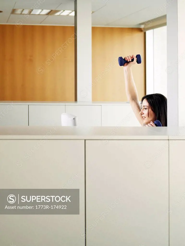Woman sitting in office lifting weights, side view