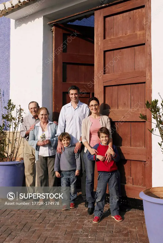 Multi-generational family standing at front door, smiling, portrait
