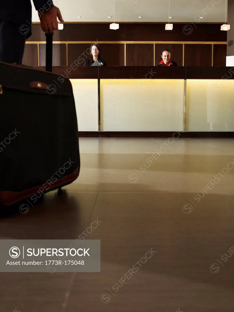 Man wheeling suitcase towards hotel reception desk, low section