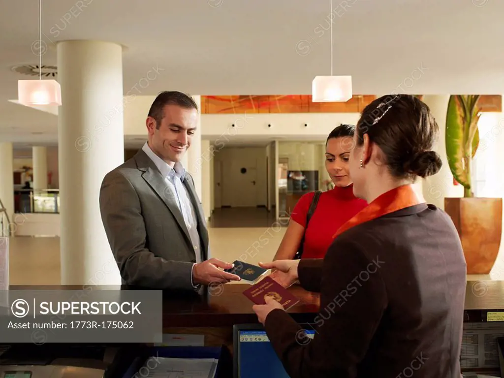 Couple handing passports to female hotel receptionist