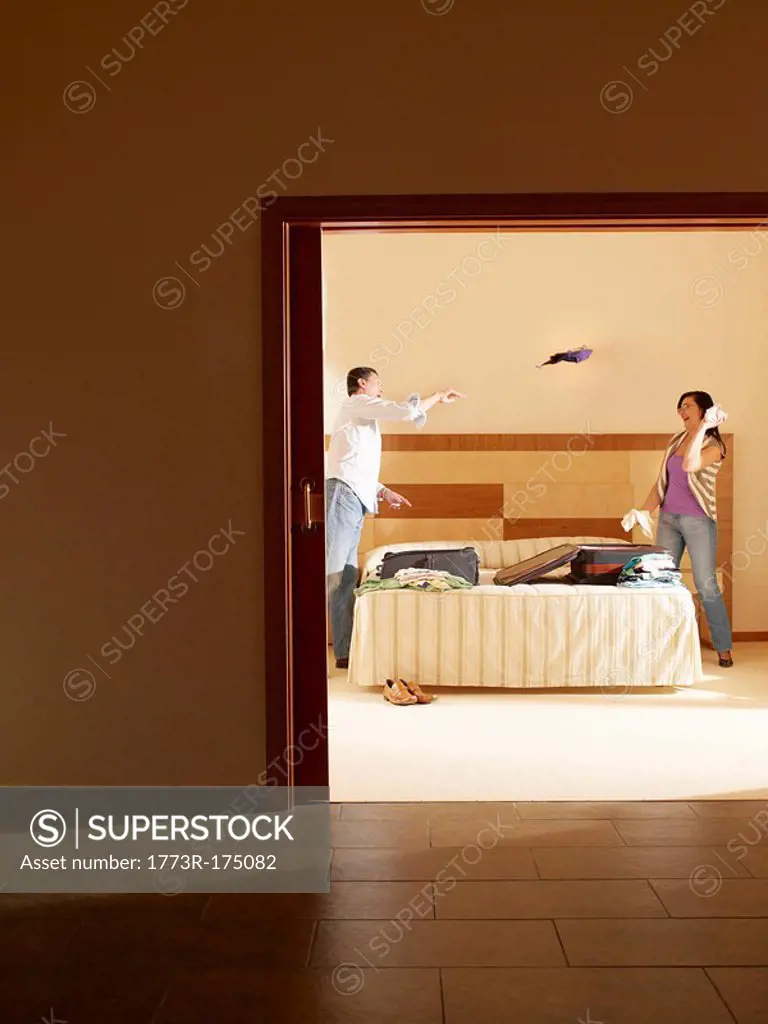 Mature couple in hotel room, man throwing clothing over bed