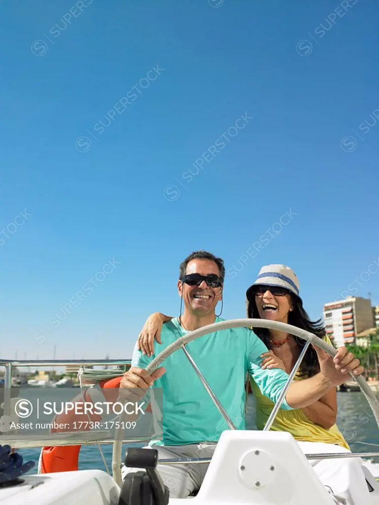 Mature couple wearing sunglasses at wheel of yacht, smiling
