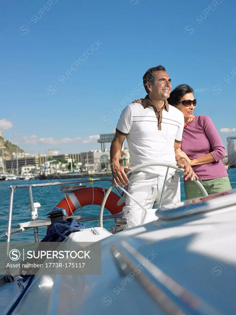Mature couple at wheel of yacht, smiling