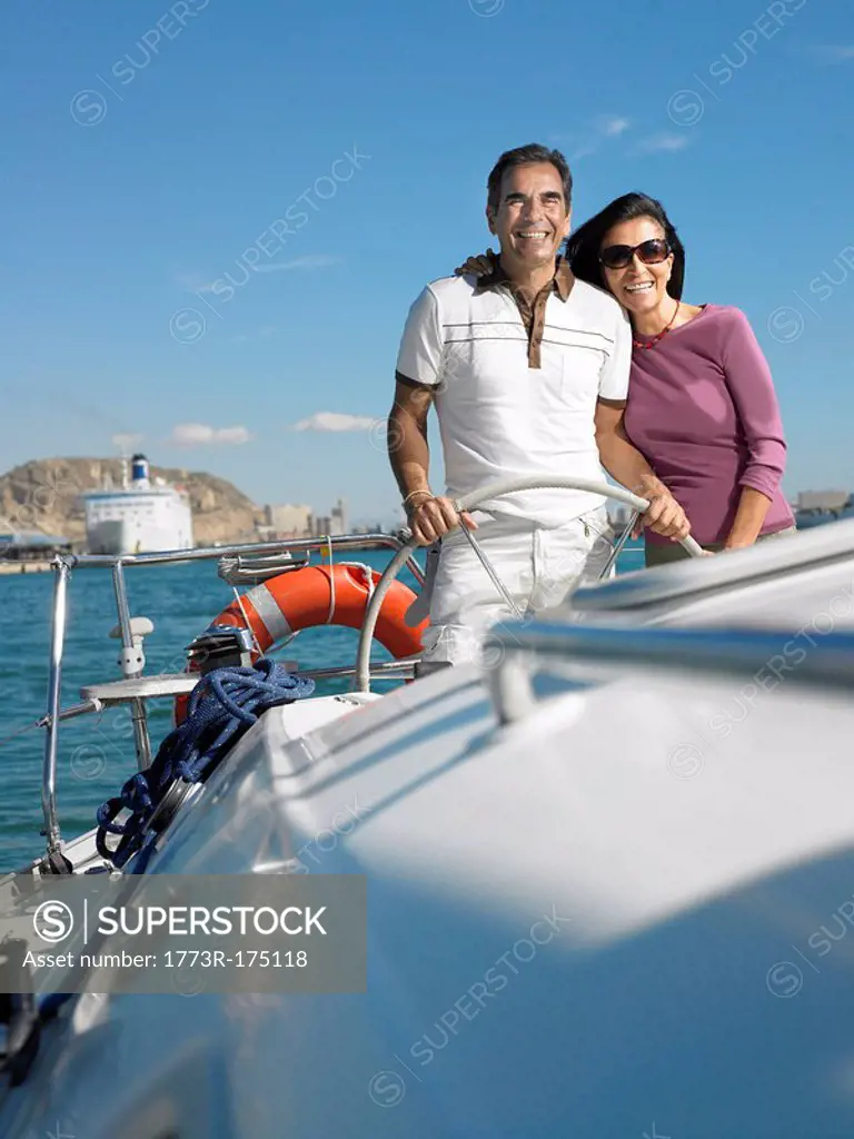 Mature couple at wheel of yacht, smiling