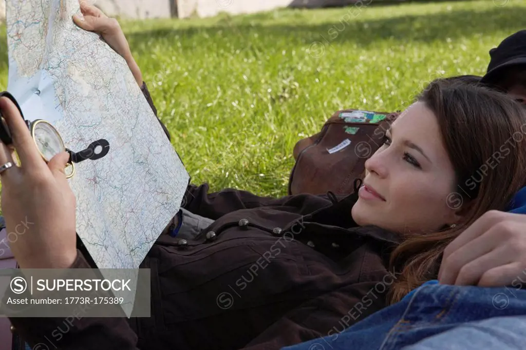 Woman smiling holding map reclining on sleeping man in a park