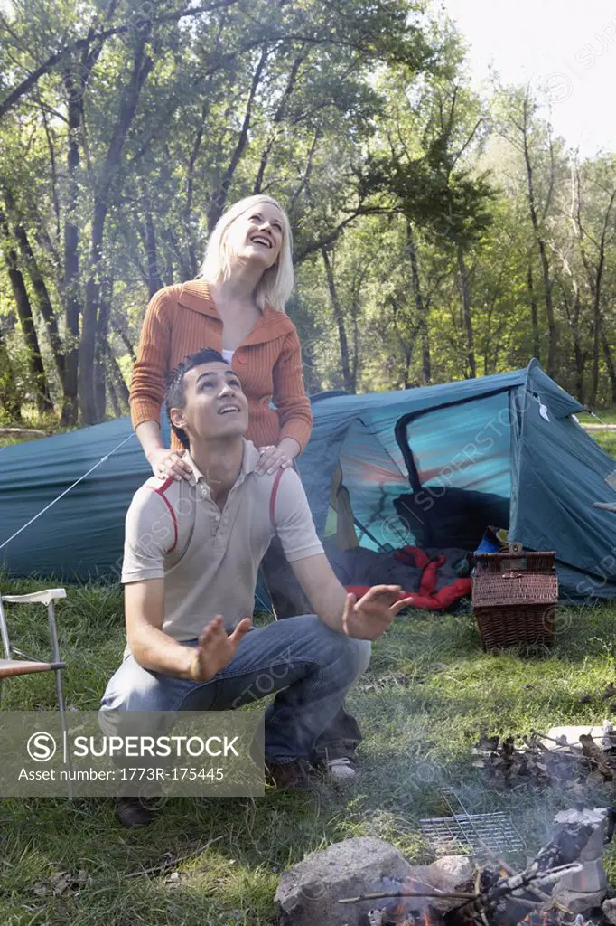 Couple at campsite looking up at smoke from the fire pit smiling