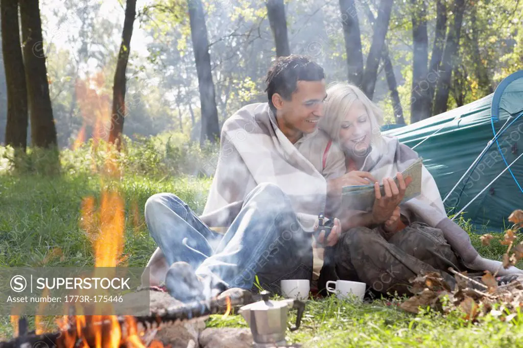 Couple sitting at campsite looking at map by the fire smiling