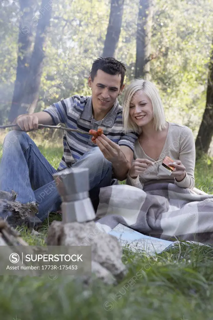 Couple at campsite cooking hot dogs and smiling