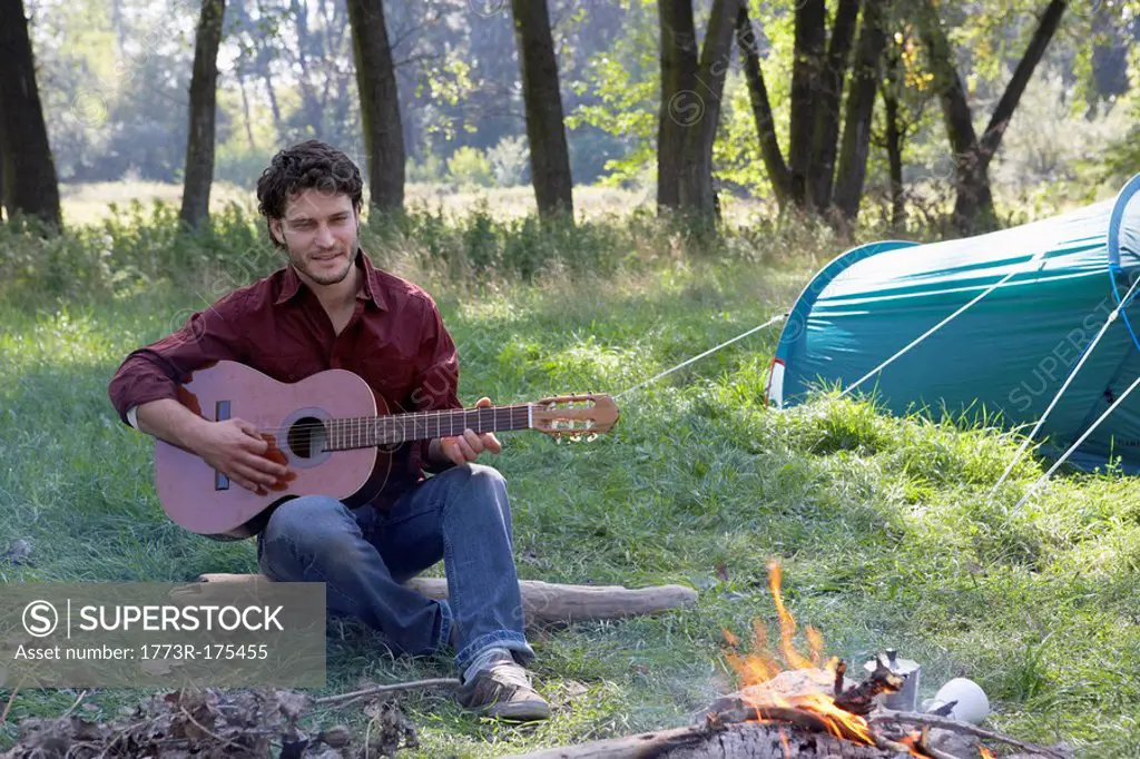 Man at campsite playing guitar and smiling