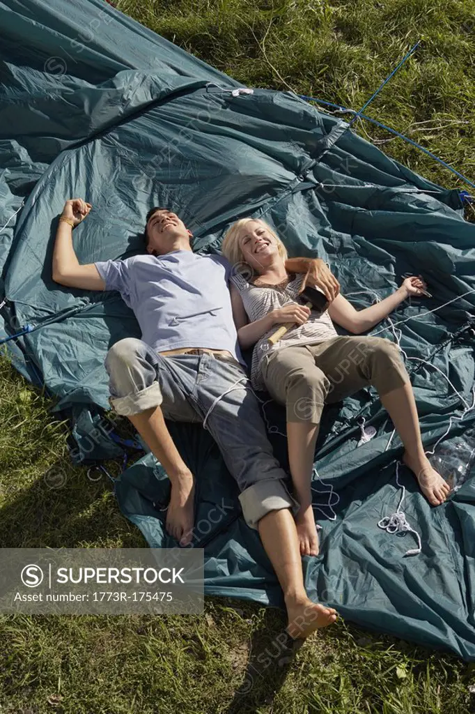 Couple lying on unraised tent smiling with the woman holding mallet