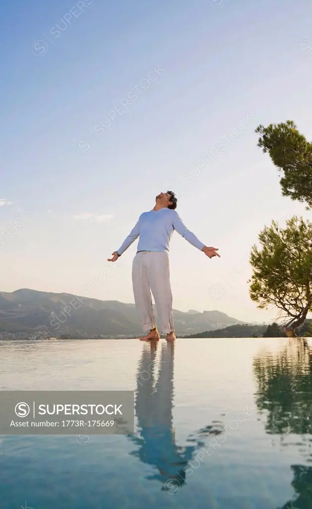 Man stands in open space sky and reflective pool arms out