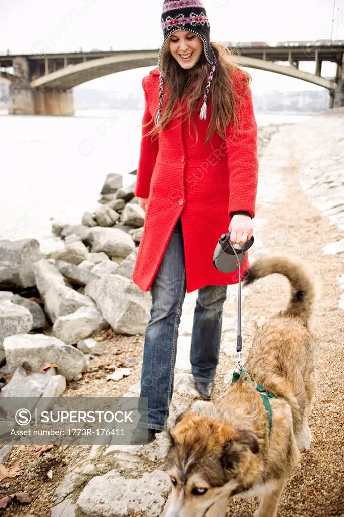 Young woman walking dog on lead by river, smiling