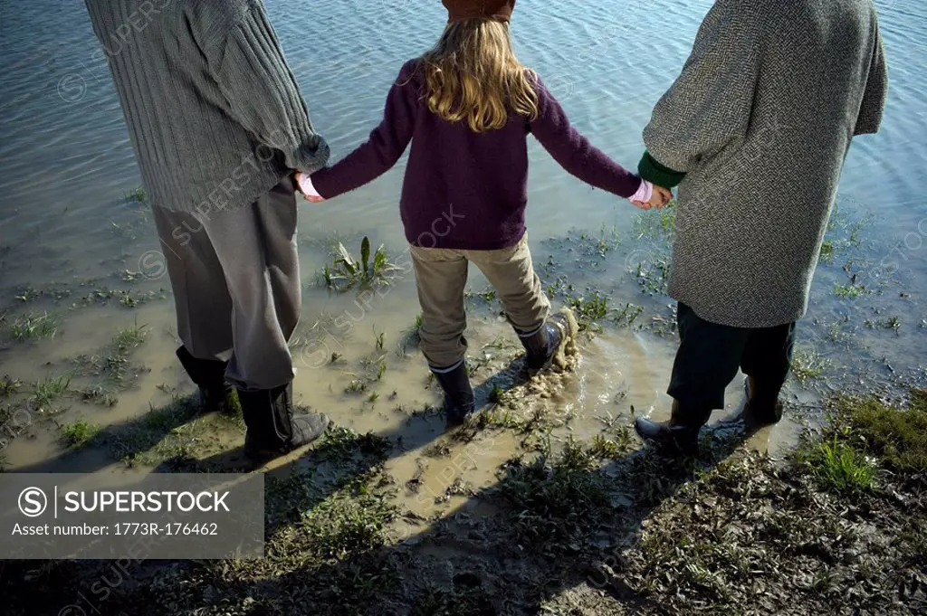 Grandparents holding hands with granddaughter 10-12 by river