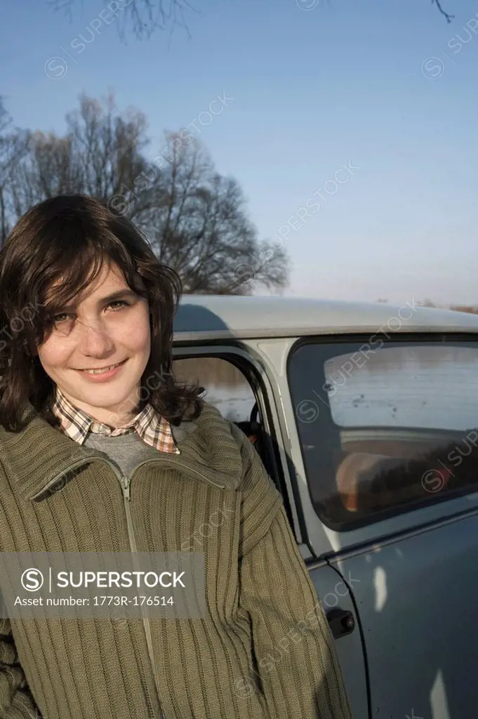 Boy 12-14 standing by car, smiling, portrait