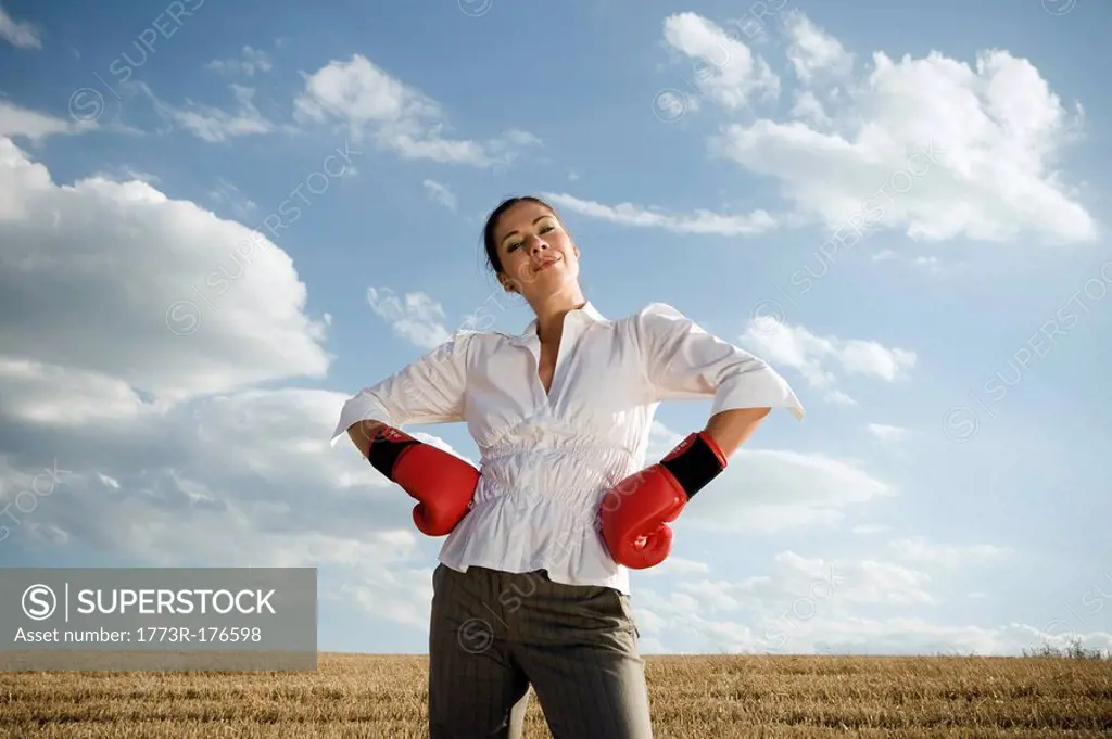 Businesswoman in wheat field wearing boxing gloves