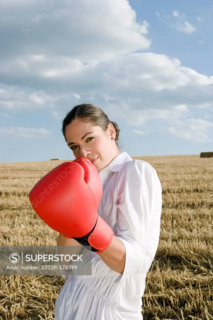 Businesswoman in wheat field wearing boxing gloves
