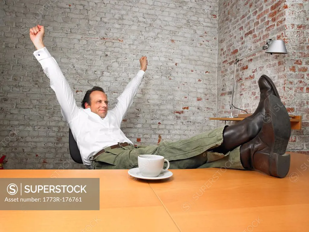 Businessman stretching with feet on desk ,