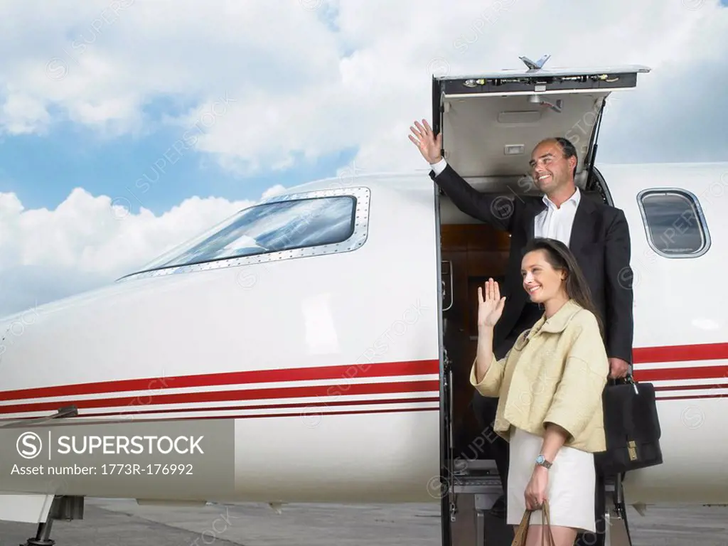 Couple exiting private jet while waving
