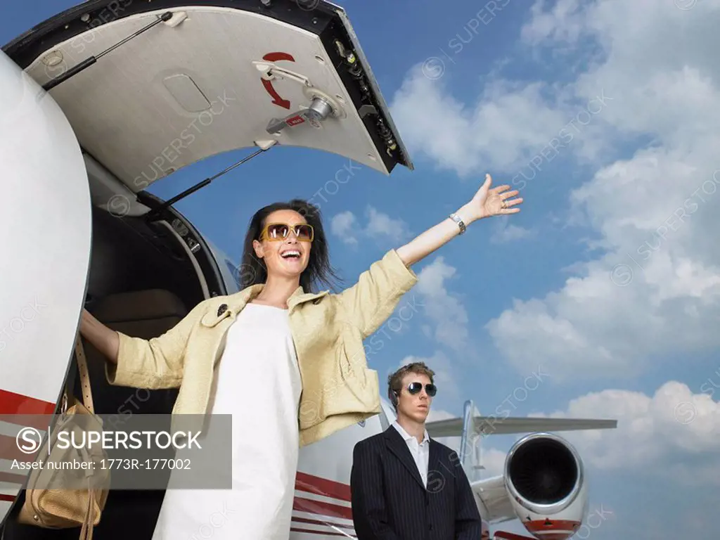 Smiling woman exiting private jet with bodyguard
