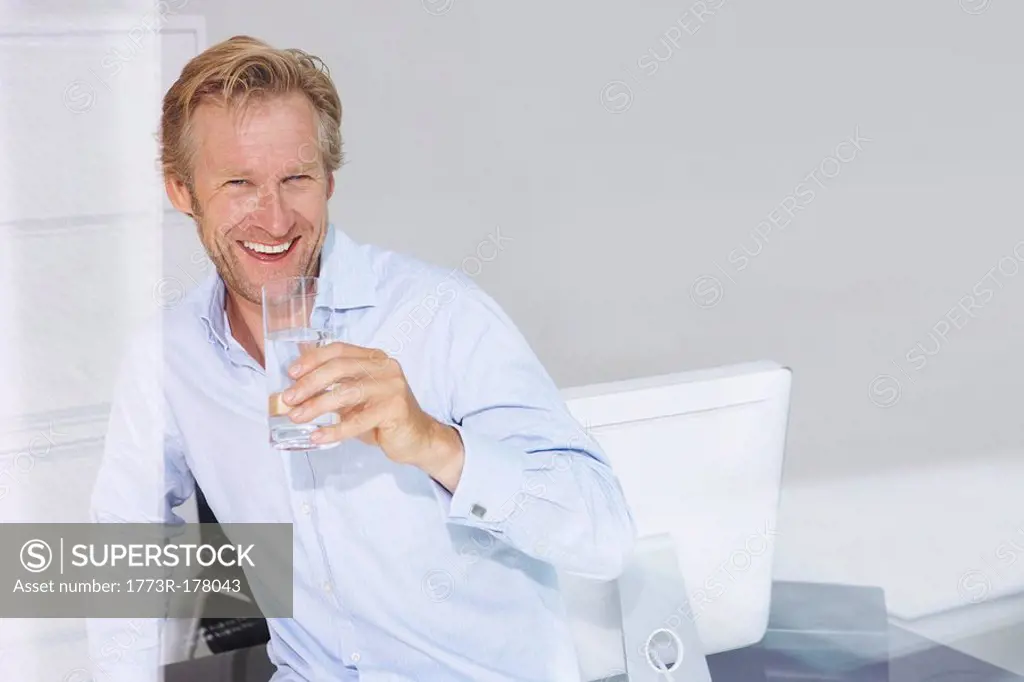 Man in office with glass of water smiling with reflections