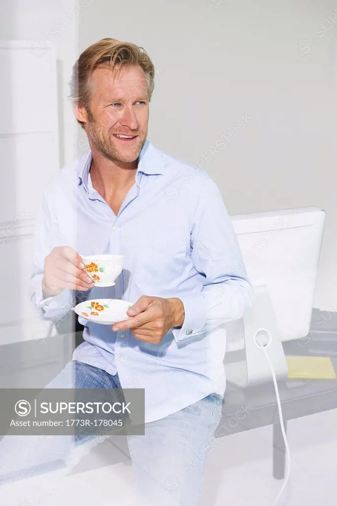Man in office with cup of tea smiling with reflections