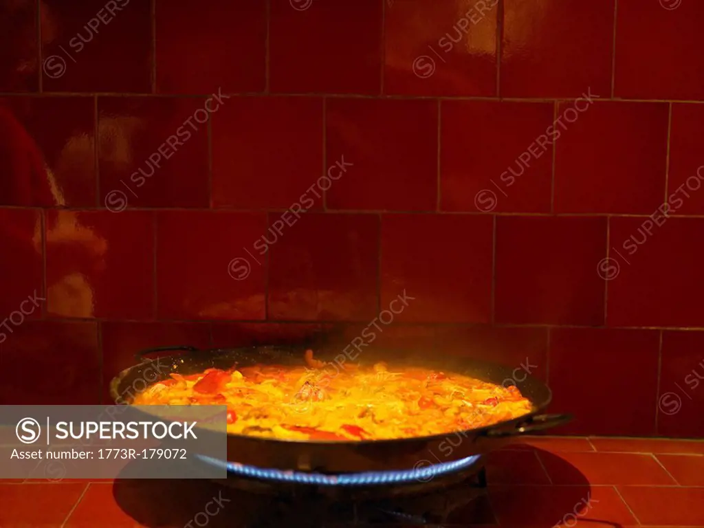 Steaming dish of paella cooking on gas stove