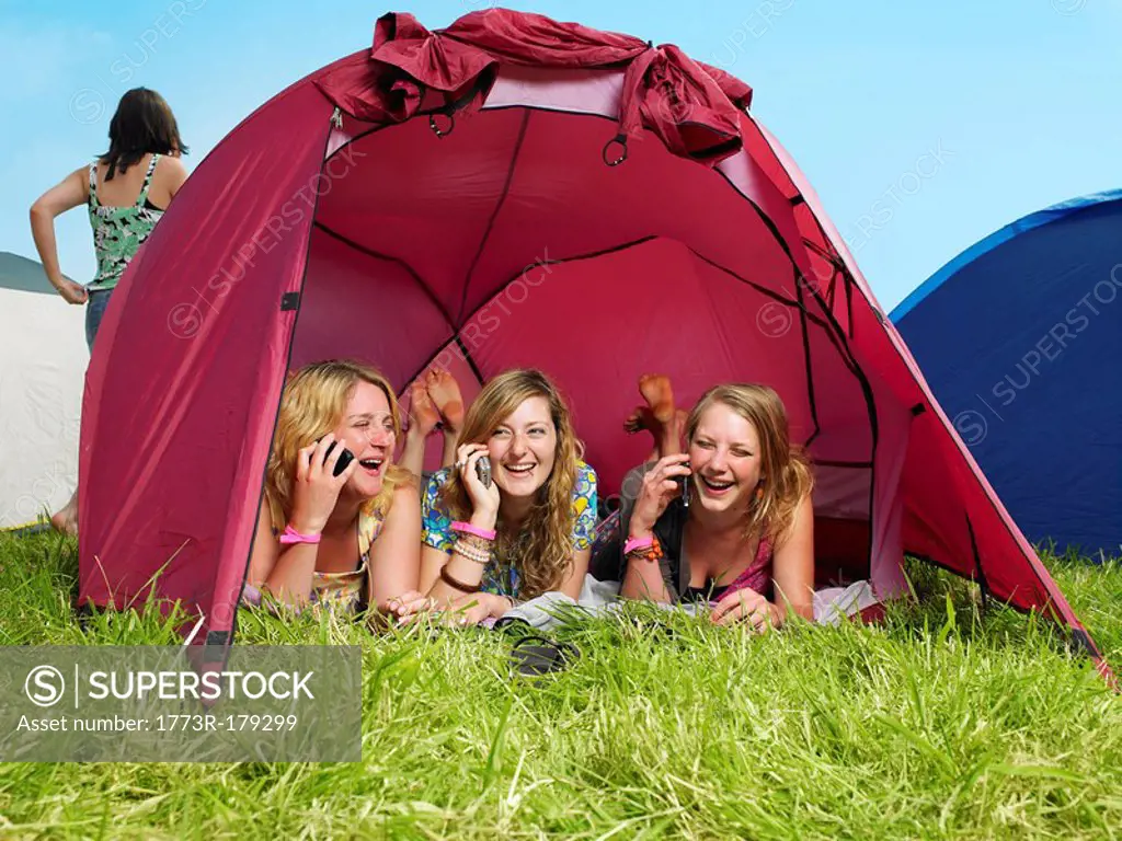 Three girls lying in tent talking on mobile phones