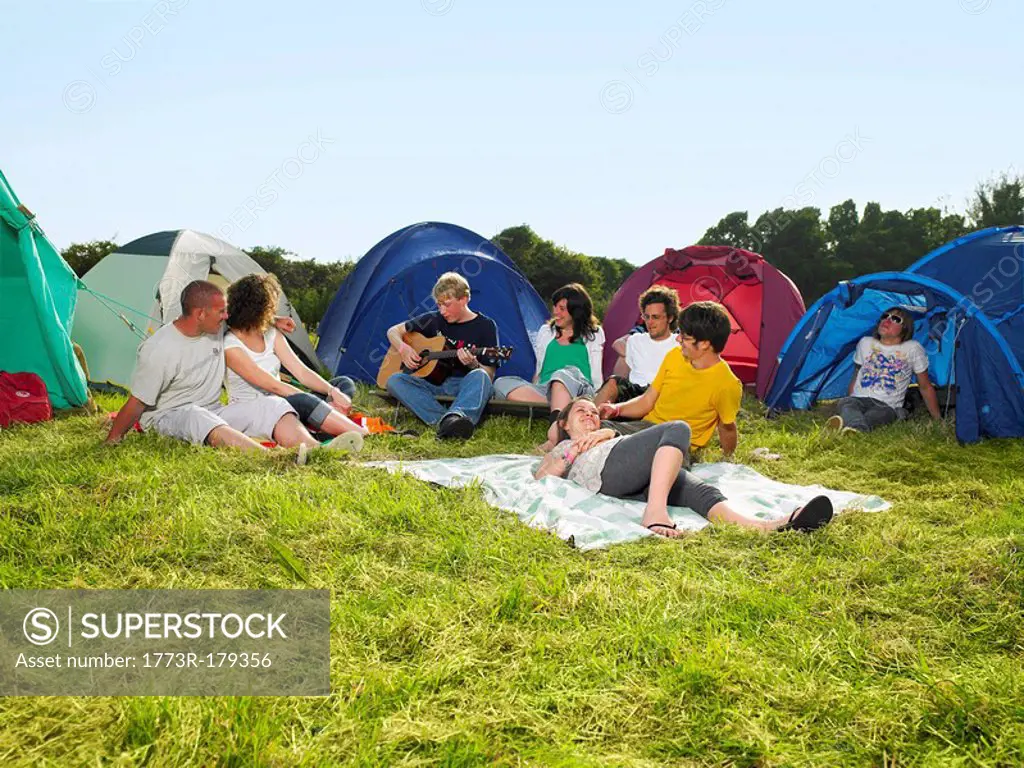 Group sitting outside tents one playing guitar