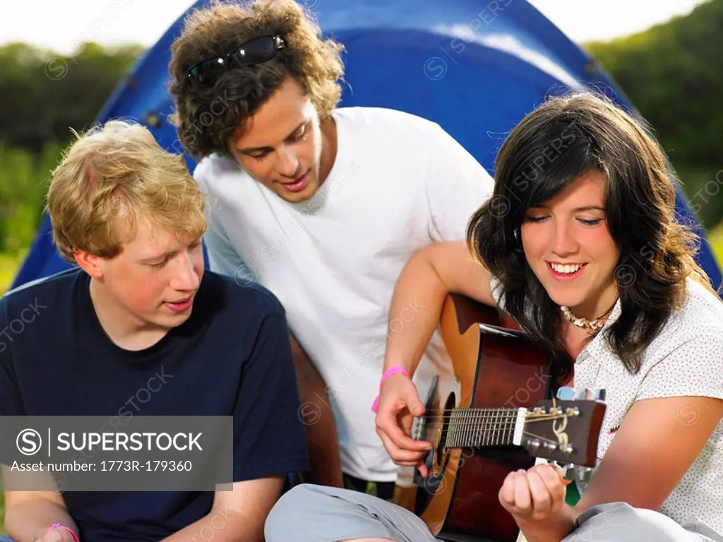 Two young men watching girl playing guitar