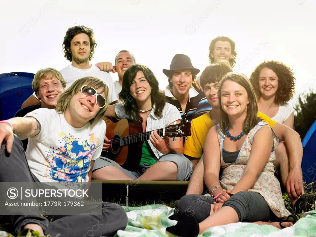 Group smiling at camera sitting outside tents with guitar