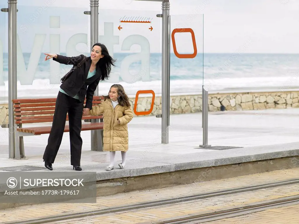 Mother and daughter 6-8 waiting at tram stop on coast