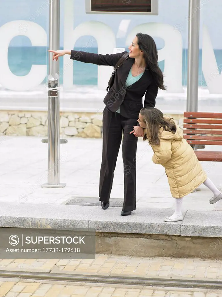 Woman and little girl 6-8 waiting at tram stop, woman pointing Alicante, Spain