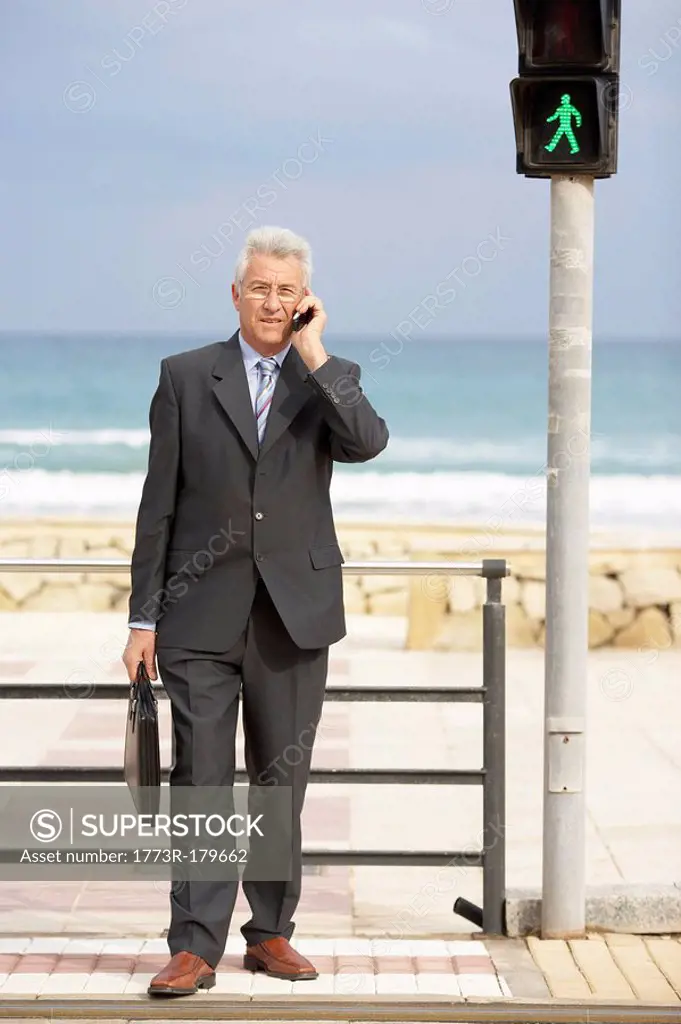 Senior businessman using mobile phone at pedestrian crossing