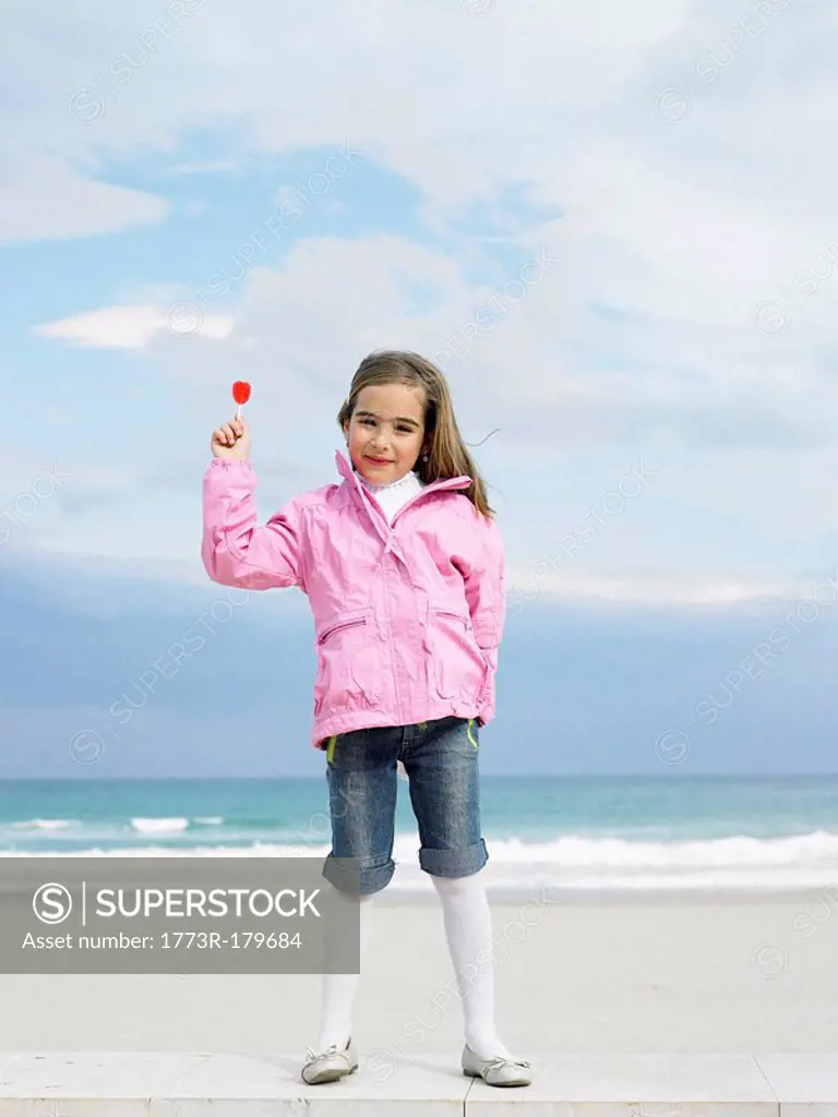 Young girl 6-8 holding lollipop in front of sea, portrait Alicante, Spain