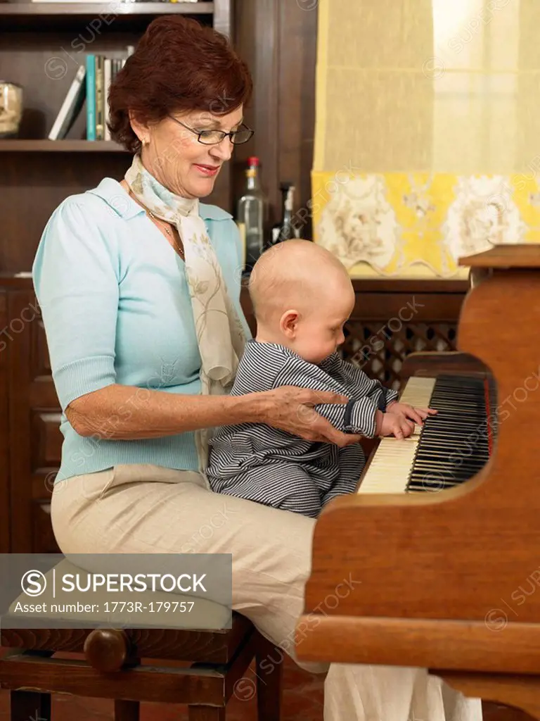 Senior grandmother playing piano with baby grandson 1-3 months