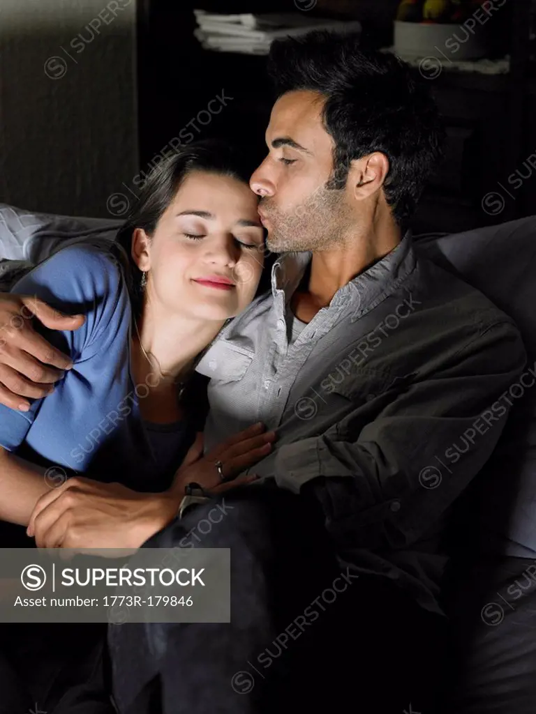 Young couple relaxing on sofa, man kissing woman