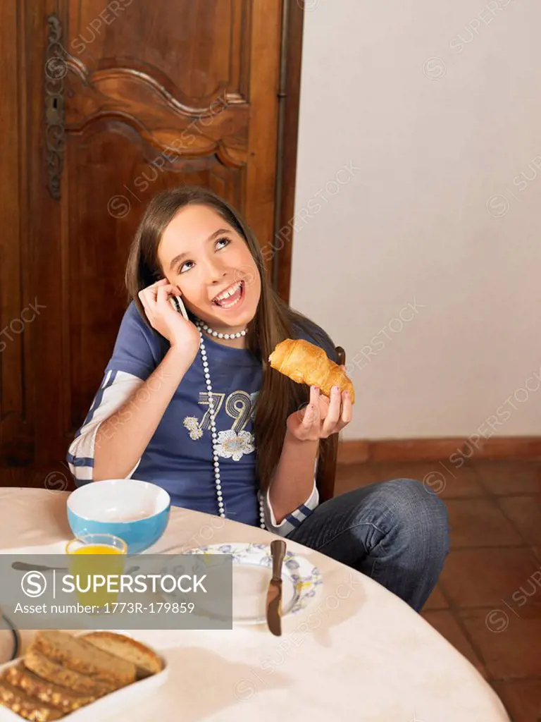 Girl 12-14 talking on phone at breakfast table
