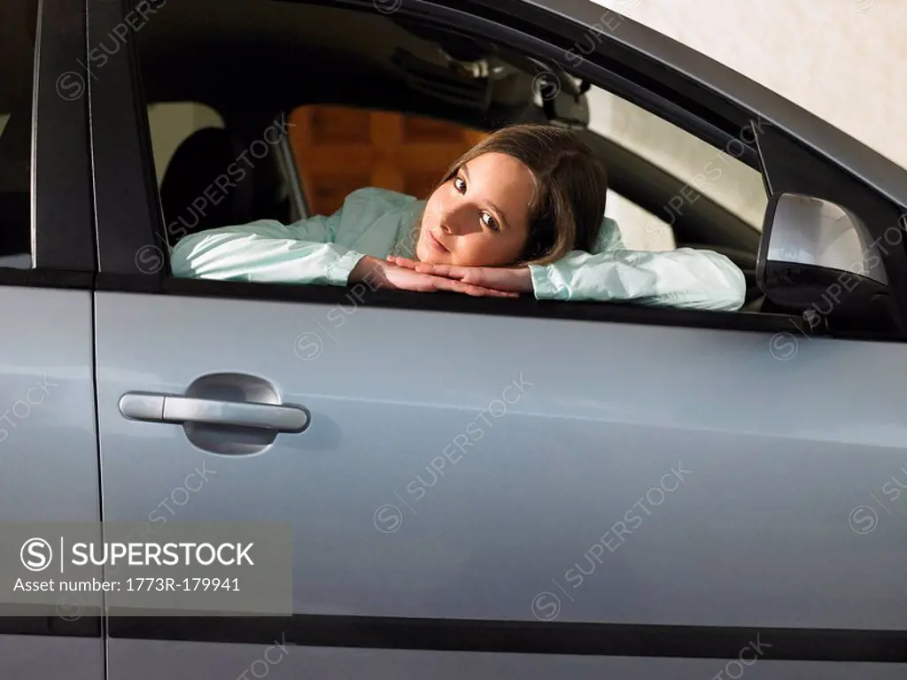 Girl 12-14 sitting in car, leaning on open window, portrait