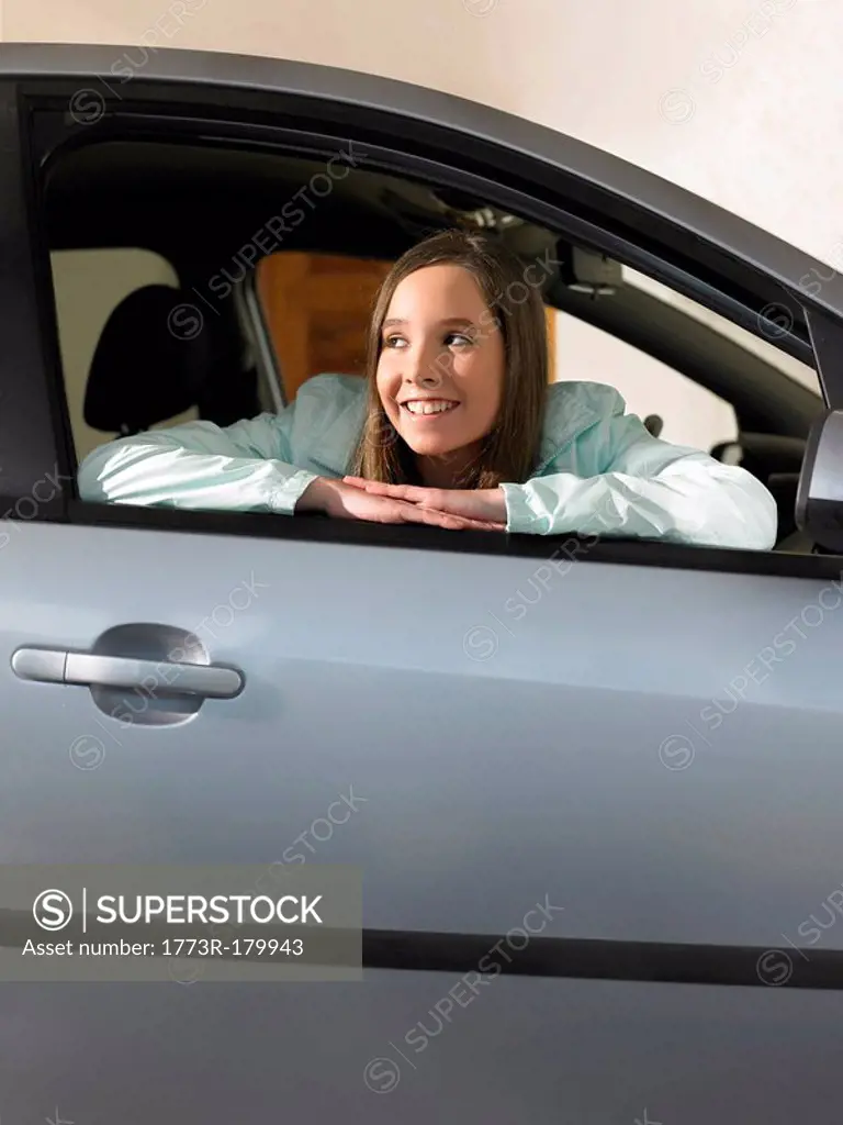 Girl 12-14 sitting in car, leaning out of window, smiling