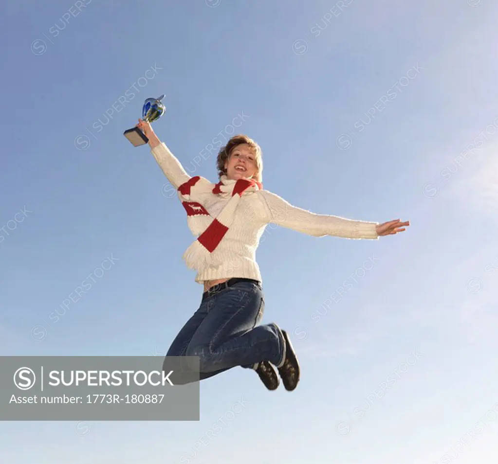 Woman jumping, holding trophy